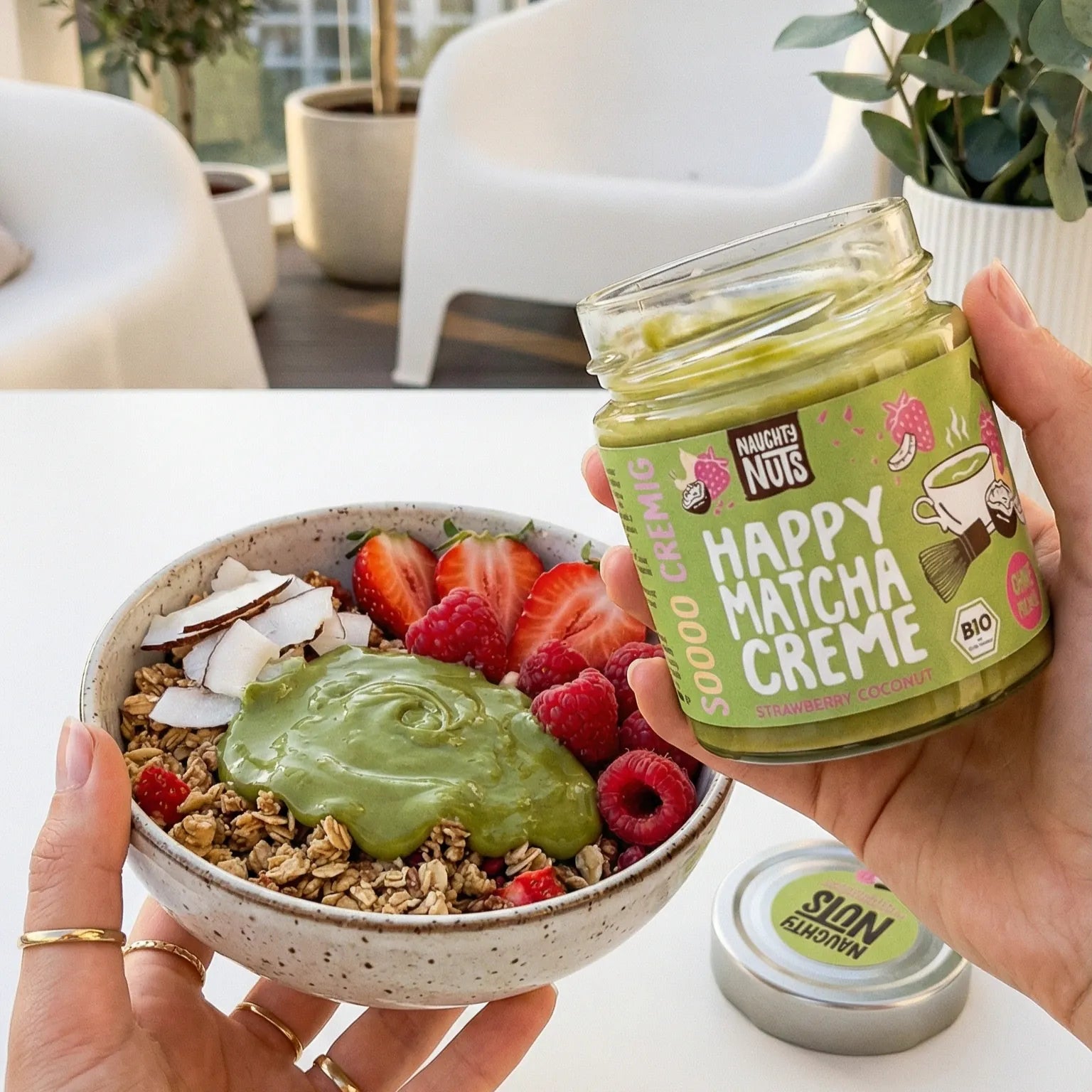 Happy Matcha Creme Glas über einer Schüssel mit Müsli, Erdbeeren, Himbeeren und Kokosnussflocken