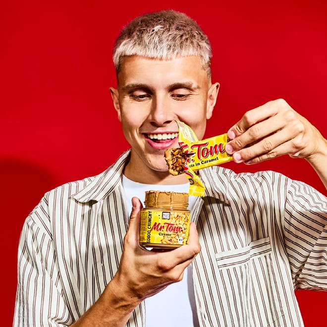 Mann hält Mr Tom Creme Glas und Mr Tom Riegel vor rotem Hintergrund