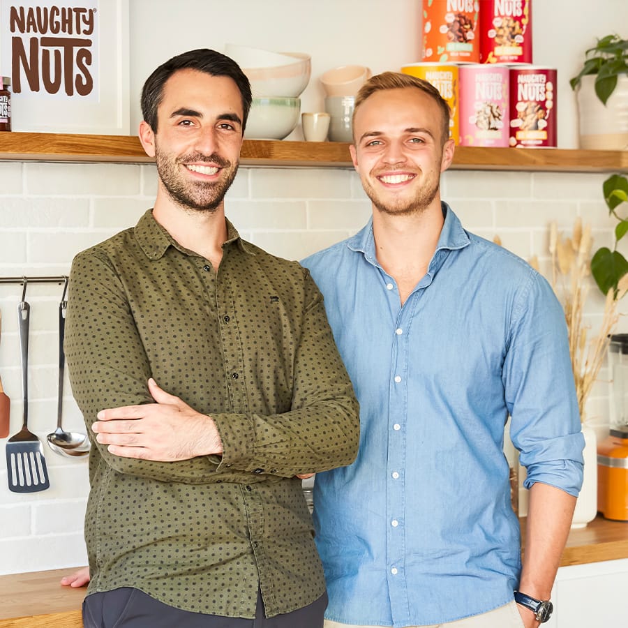 Zwei Männer in einer Küche mit Naughty Nuts Produkten im Hintergrund